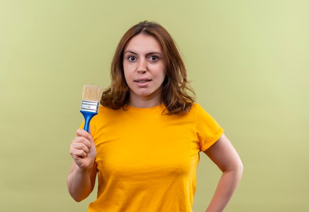 Confident young casual woman holding paint brush on isolated green space with copy space