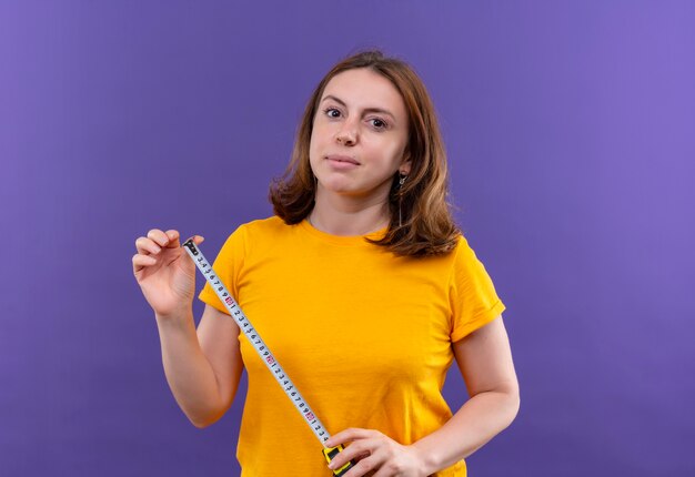 Confident young casual woman holding tape meter on isolated purple space with copy space