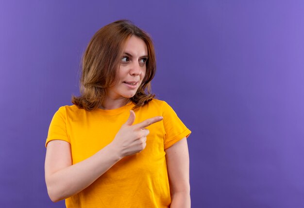 Confident young casual woman pointing and looking at right side on isolated purple space with copy space