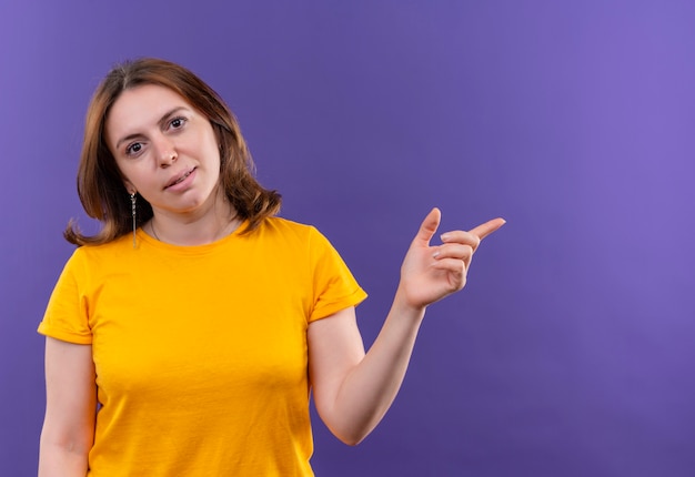 Confident young casual woman pointing at right side on isolated purple space with copy space