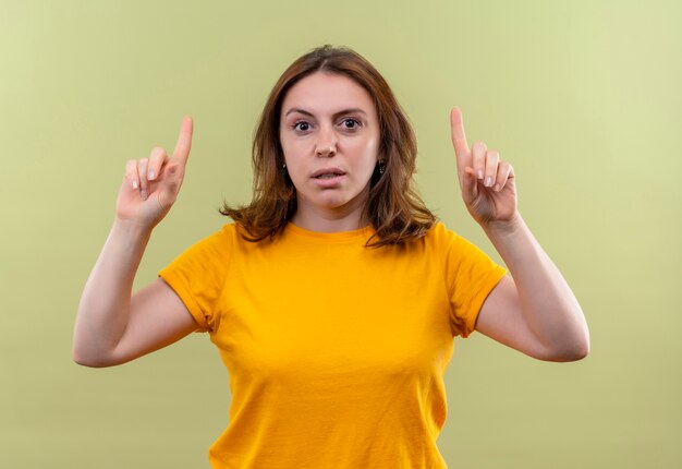 Confident young casual woman pointing up on isolated green space