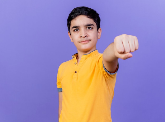 Confident young caucasian boy  stretching out fist towards isolated on purple wall with copy space