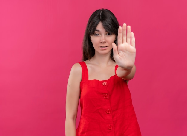 Confident young caucasian girl does stop gesture and looks at camera on isolated pink background with copy space