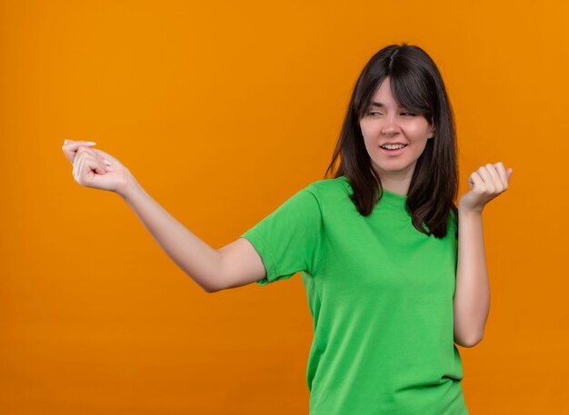 Confident young caucasian girl in green shirt pretends to call someome on isolated orange background with copy space