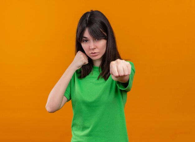 緑のシャツを着た自信を持って若い白人の女の子は、孤立したオレンジ色の背景にパンチを装います