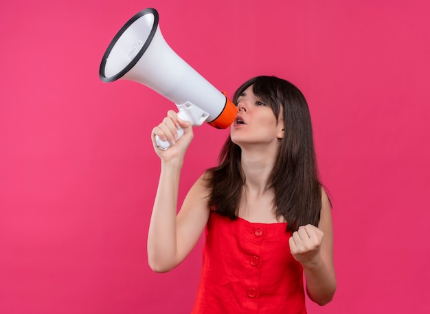 Confident young caucasian girl holding loud speaker and holding fist up on isolated pink background