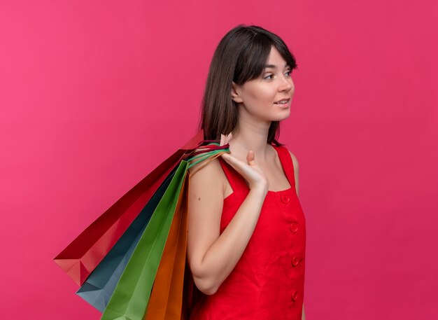 Confident young caucasian girl holds packages throwing them on shoulder on isolated pink background