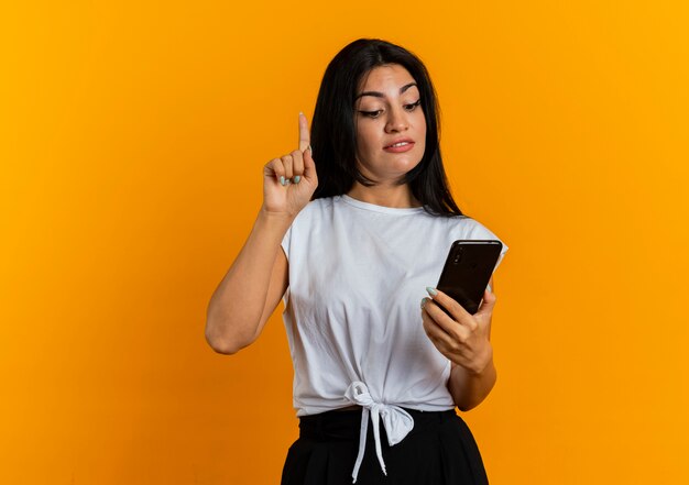Confident young caucasian girl points up looking at phone 