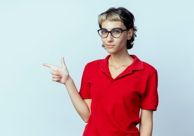 Confident young caucasian girl with pixie haircut wearing glasses and pointing at side isolated on white background