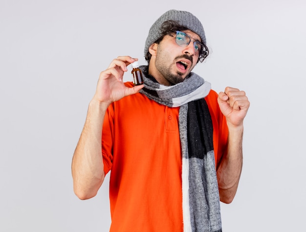 Free photo confident young caucasian ill man wearing glasses winter hat and scarf holding medicament in glass  doing be strong gesture isolated on white wall with copy space