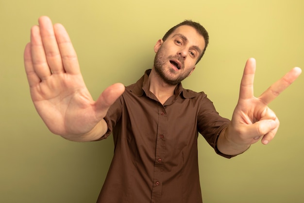 Free photo confident young caucasian man looking at camera showing seven with hands isolated on olive green background