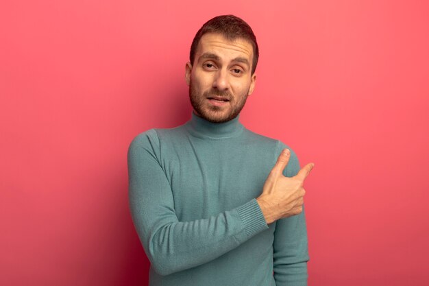 Confident young caucasian man  pointing behind isolated on crimson wall with copy space