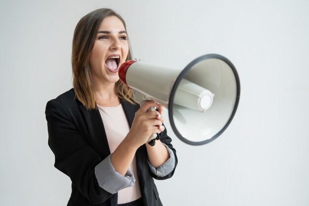 Confident young Caucasian woman shouting aside in megaphone