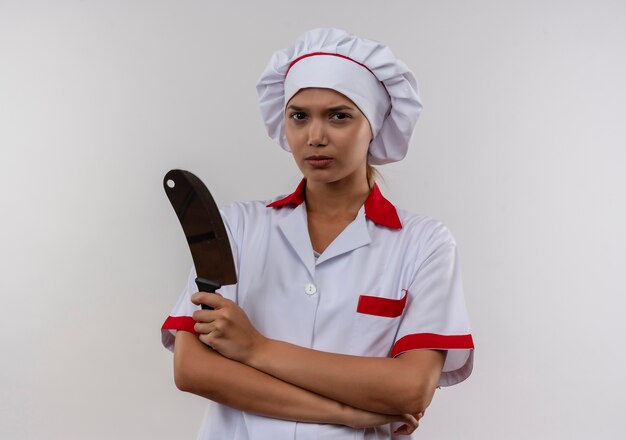 Confident young cook female wearing chef uniform crossing hands holding cleaver on isolated white wall with copy space