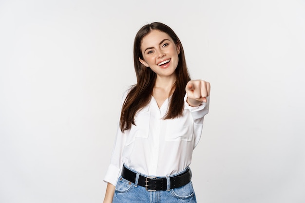 Foto gratuita fiduciosa giovane donna aziendale che punta il dito verso di te fotocamera, invitando, scegliendo, congratulandosi, in piedi su sfondo bianco