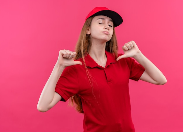 자신을 가리키고 격리 된 분홍색 공간에 윙크하는 빨간 제복을 입은 자신감이 어린 배달 소녀