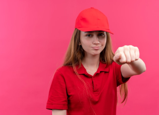 Confident young delivery girl in red uniform stretching out her fist  on isolated pink space with copy space