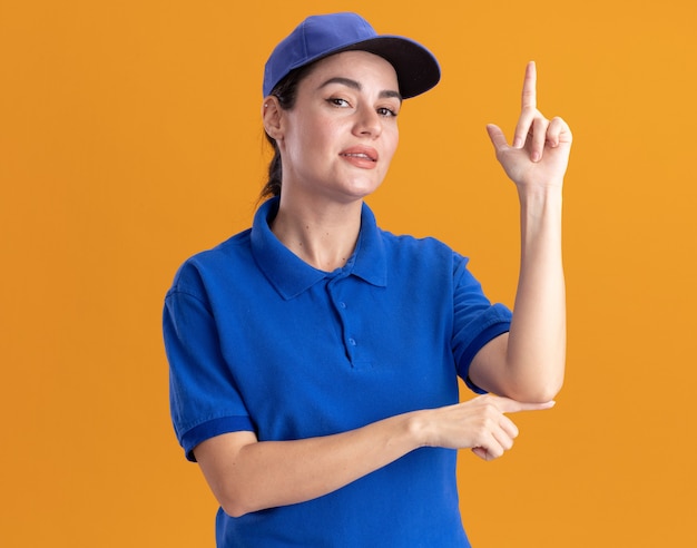 Free photo confident young delivery woman in uniform and cap pointing up