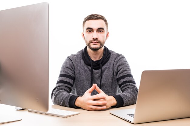 Confident young entrepreneur sitting at the table with laptop and pc, looking at camera isolated on white