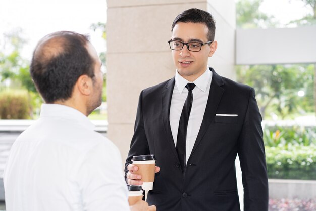 Confident young executive in glasses talking to his colleague