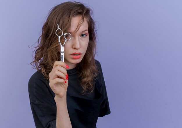 confident young female barber wearing uniform holding scissors looking at front