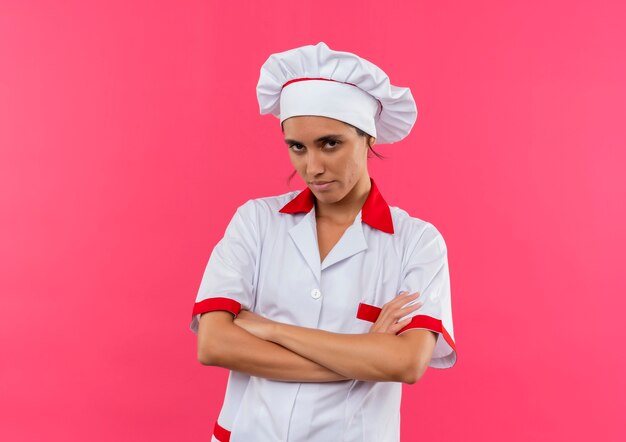  confident young female cook wearing chef uniform crossing hands on isolated pink wall with copy space