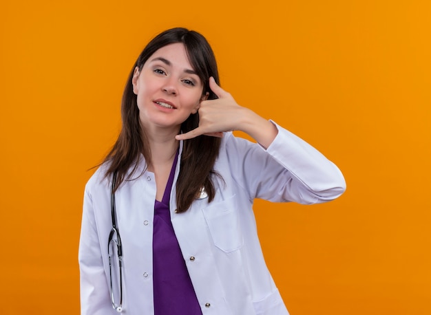 聴診器のジェスチャーで医療ローブの自信を持って若い女性医師は、コピースペースと孤立したオレンジ色の背景に手で呼び出します