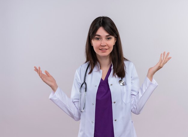 Confident young female doctor in medical robe with stethoscope holds hands up on isolated white background with copy space