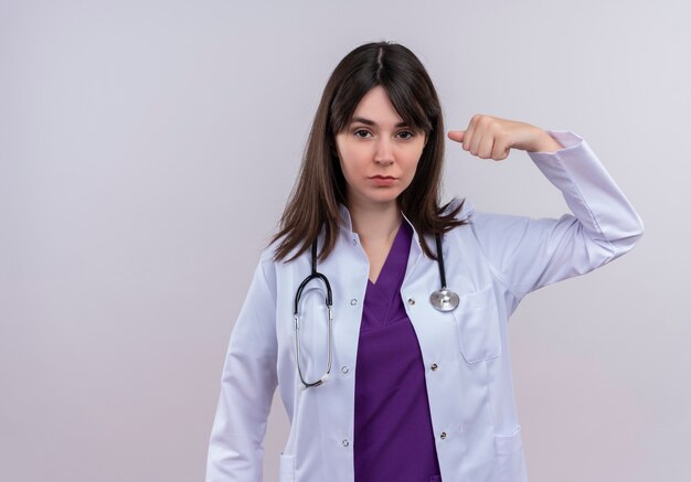 Confident young female doctor in medical robe with stethoscope points at herself on isolated white background with copy space