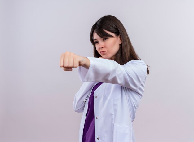 Confident young female doctor in medical robe with stethoscope pretends to pounch on isolated white background with copy space