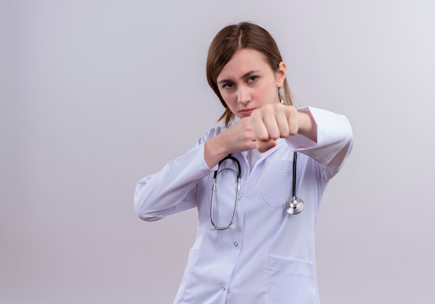 Уверенная молодая женщина-врач в медицинском халате и стетоскопе делает боксерский жест с копией пространства