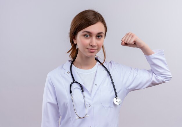 Confident young female doctor wearing medical robe and stethoscope doing strong gesture 