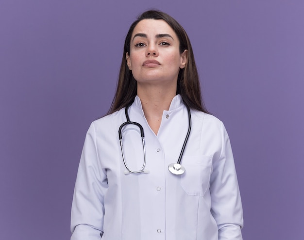 복사 공간이 있는 보라색 벽에 격리된 청진기가 달린 의료 가운을 입은 자신감 있는 젊은 여성 의사