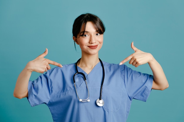 Fiduciosa giovane dottoressa che indossa uno stetoscopio fitto uniforme isolato su sfondo blu