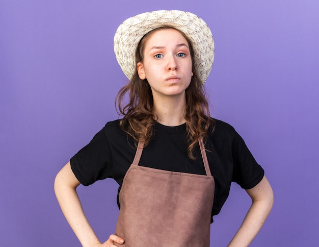 Foto gratuita fiducioso giovane giardiniere femminile che indossa cappello da giardinaggio mettendo le mani sui fianchi