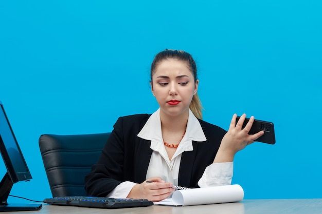 Confident young girl sitting at office and holding her phone