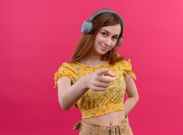 Confident young girl wearing headphones and pointing  on isolated pink space with copy space