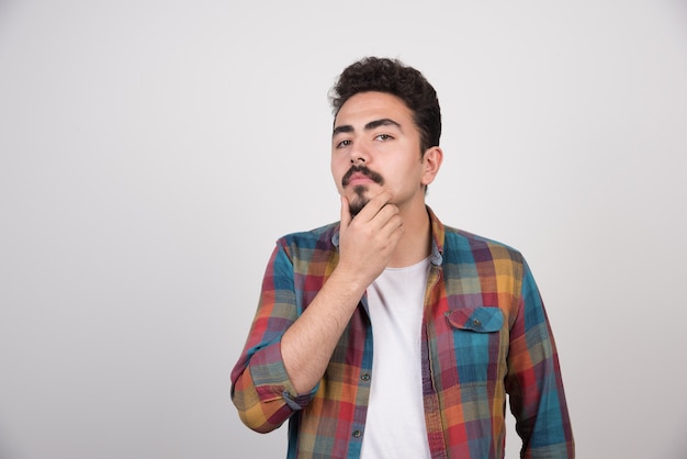 Confident young guy holding his hand to his chin and think.