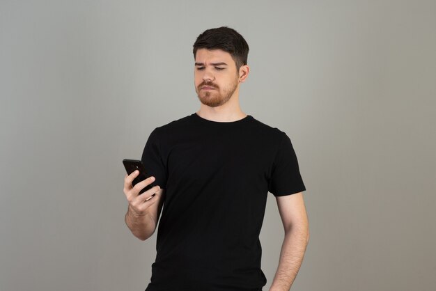 A confident young guy holding a phone and looking at it on a grey.
