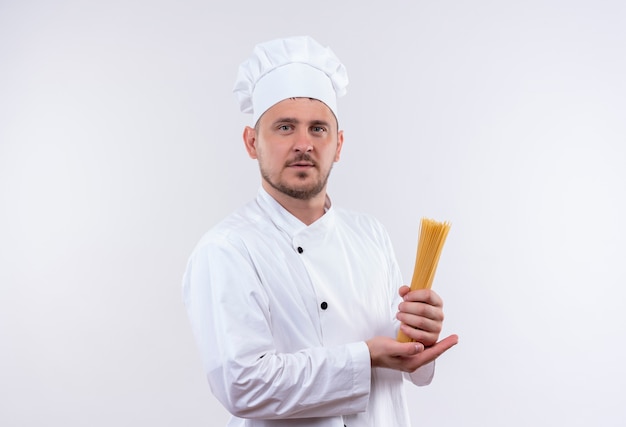 Confident young handsome cook in chef uniform holding spaghetti isolated on white wall