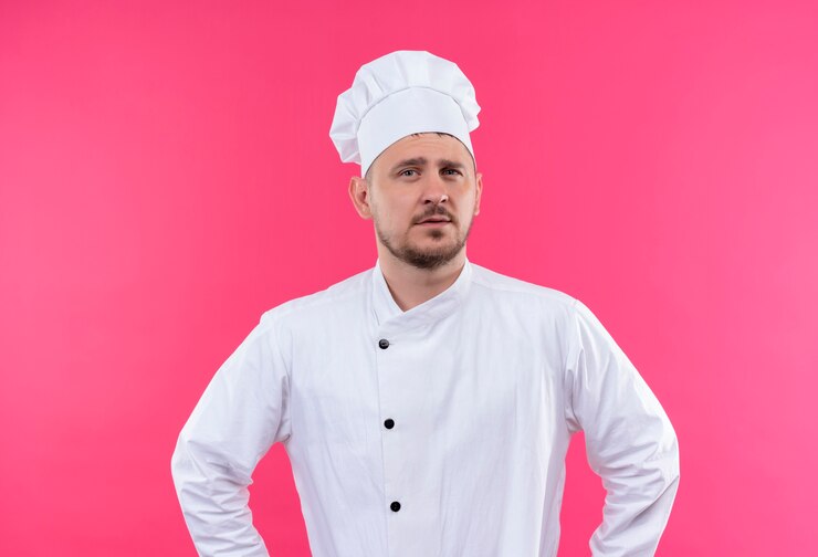 Free Photo confident young handsome cook in chef uniform isolated on pink wall
