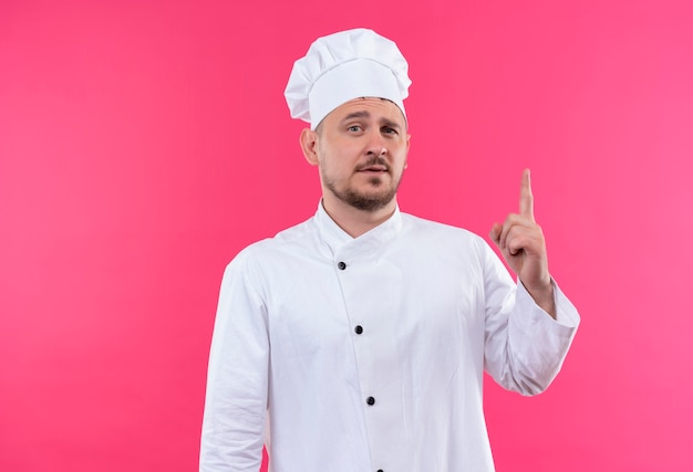 요리사 유니폼에 자신감이 젊은 잘 생긴 요리사는 분홍색 벽에 고립 가리키는