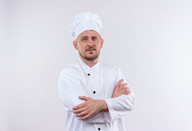 白い壁に閉じた姿勢で立っているシェフの制服を着た自信のある若いハンサムな料理人