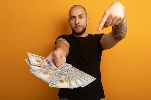 Confident young handsome guy wearing black shirt holding and points at cash