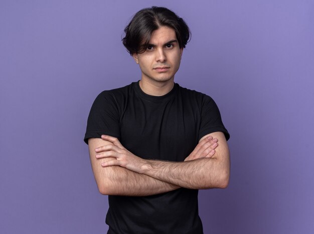 Confident young handsome guy wearing black t-shirt crossing hands isolated on purple wall