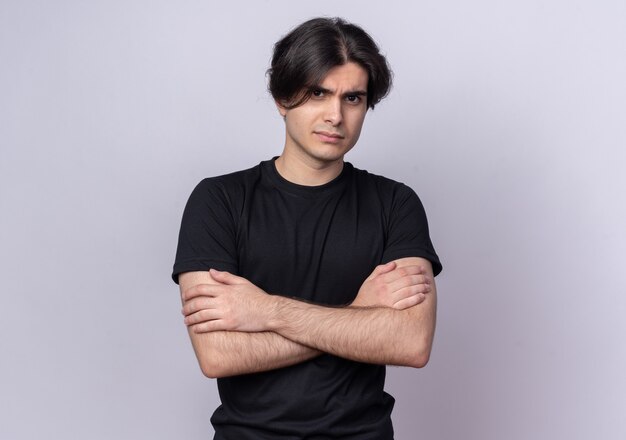 Confident young handsome guy wearing black t-shirt crossing hands isolated on white wall