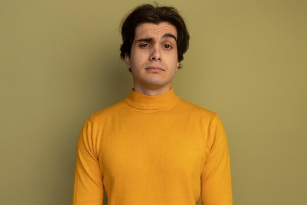 Confident young handsome guy wearing yellow turtleneck sweater isolated on olive green wall