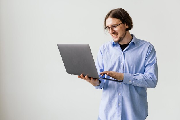 Уверенный молодой красивый мужчина в рубашке держит ноутбук и улыбается, стоя на белом фоне