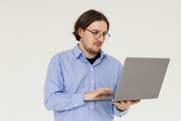 Confident young handsome man in shirt holding laptop and smiling while standing against white background
