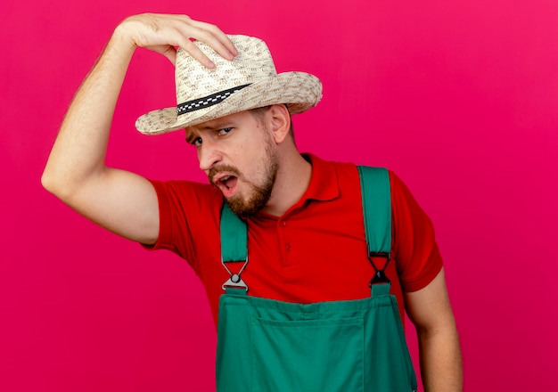 Confident young handsome slavic gardener in uniform and hat looking touching his hat 